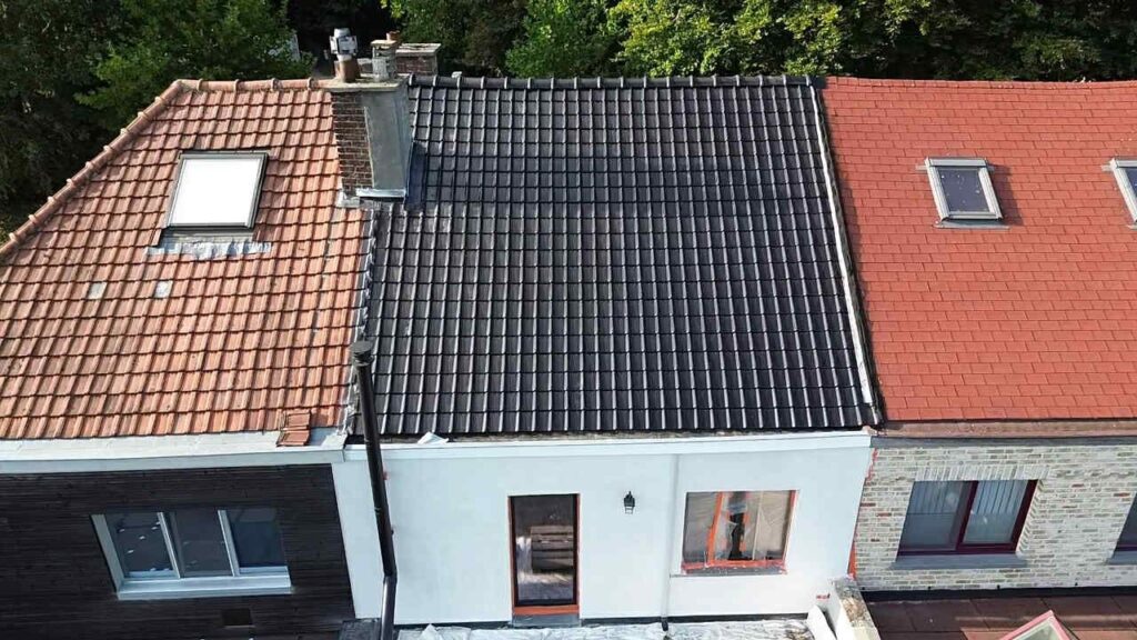 Luchtfoto van een vernieuwd zwart pannendak op een rijwoning tussen oranje daken